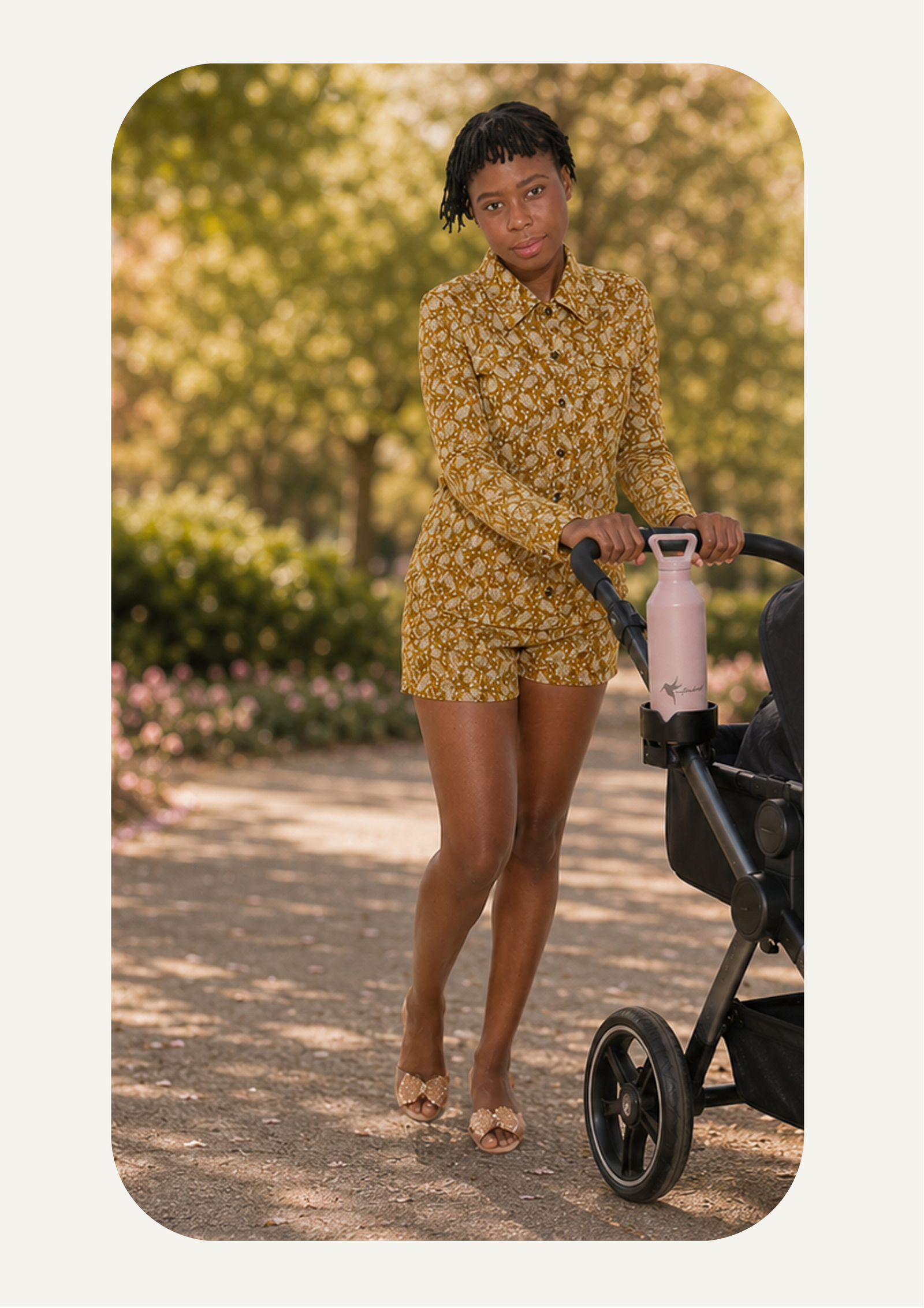 Woman in our dijon colored floral outfit pushing a stroller outdoors with her pink hydration water bottle in the cup holder
