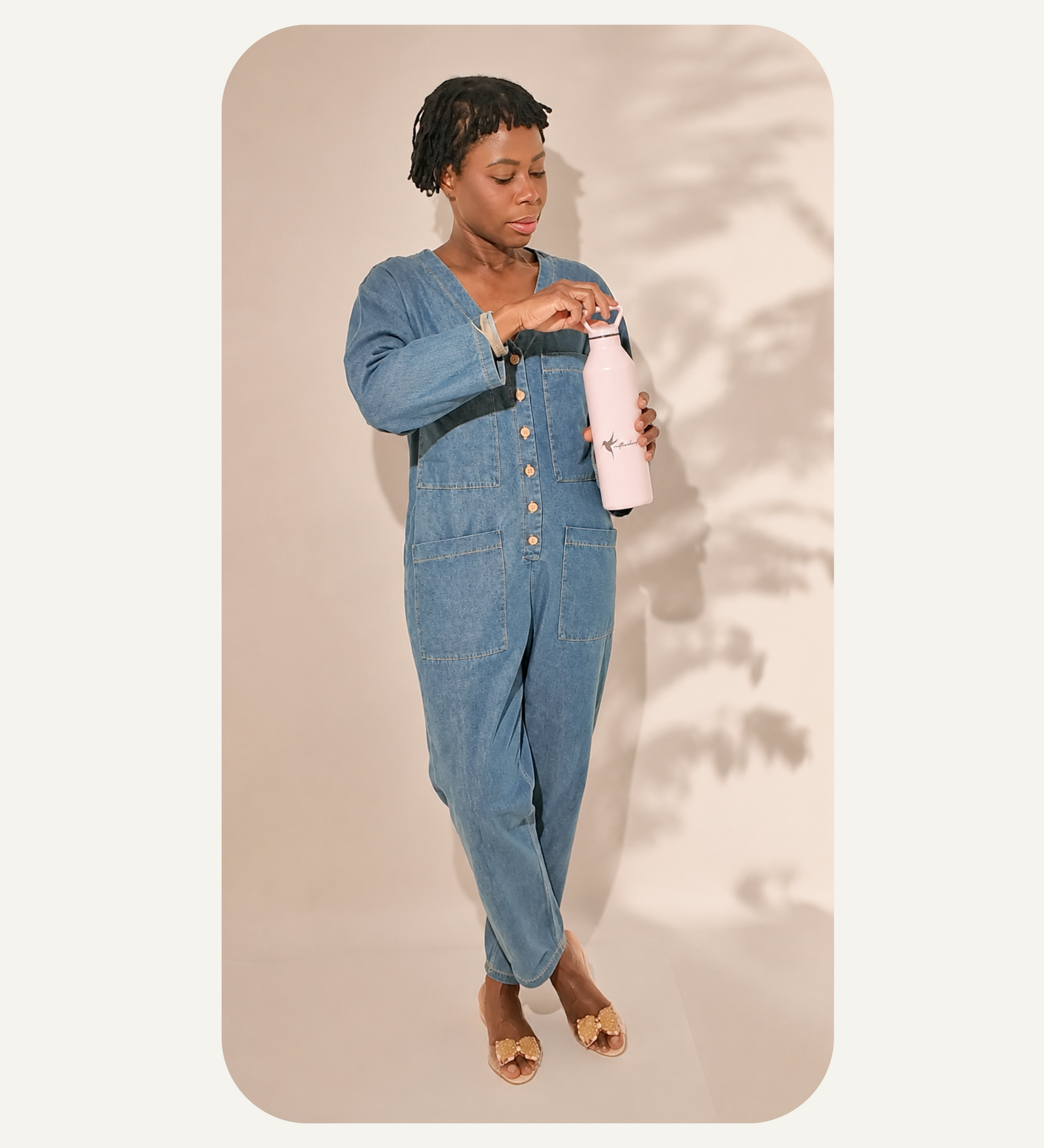 Woman in our relaxed fit denim jumpsuit holding our pink hydration bottle.